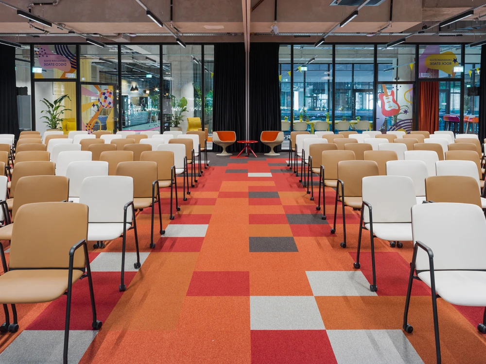 Blick durch die Crossover Stage im Smartvillage B-NK mit bunter Teppichgestaltung und Stuhlreihen