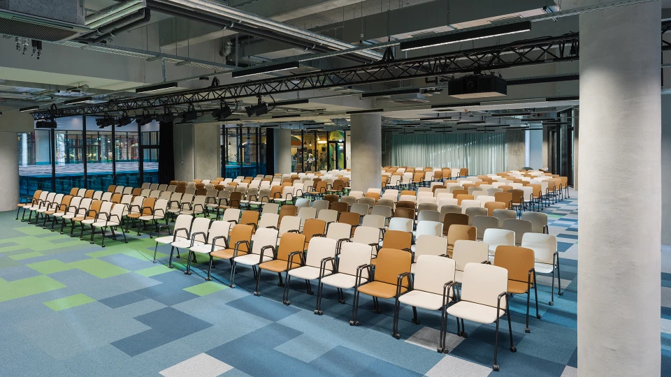 View of a seated event area with a focus on modern ceiling design featuring lighting technology and suspended elements.