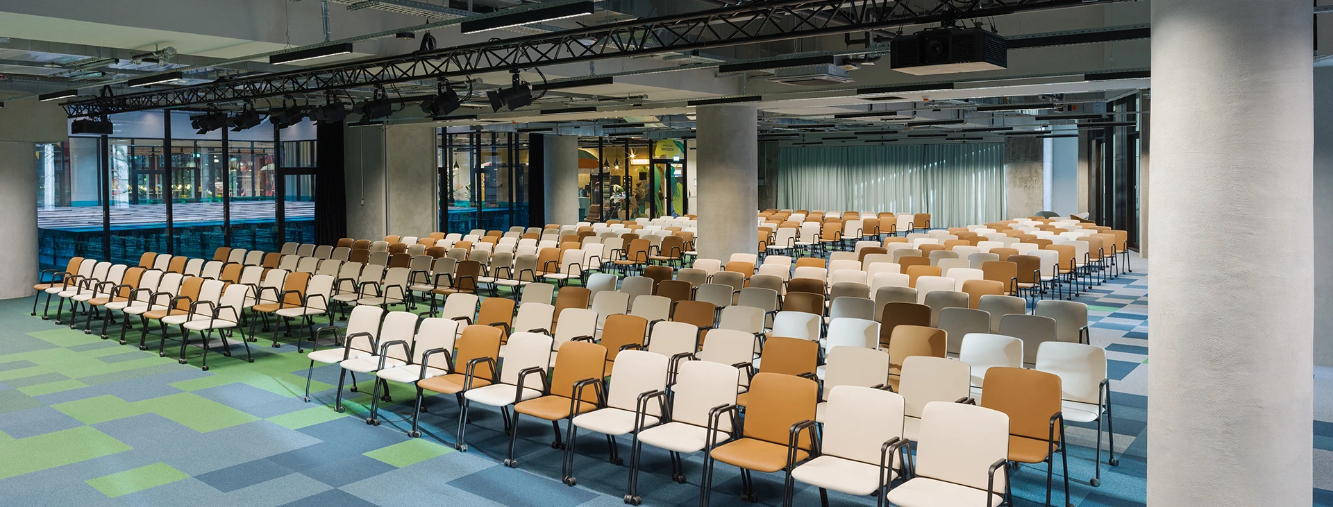 Blick auf die bestuhlte Eventfläche mit Sicht auf moderne Deckenkonstruktion mit Lichttechnik und abgehängten Elementen.