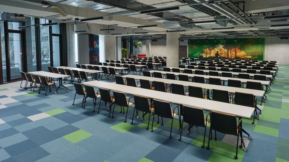 Classroom-style event space with white tables, black chairs, and carpeted flooring featuring a geometric pattern.