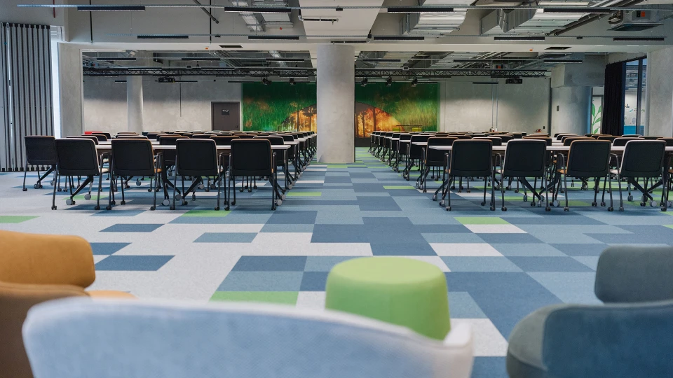 Low camera angle view over comfortable seating towards rows of chairs leading to a stage with a nature projection.