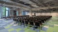 Modern, spacious conference hall with rows of black chairs, green-blue checkered carpet, and exposed ceiling installations