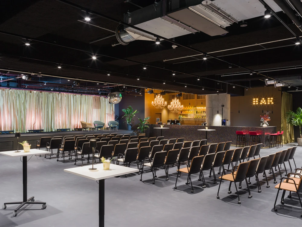 Modern event hall with rows of black chairs, an illuminated bar in the background, and decorative elements