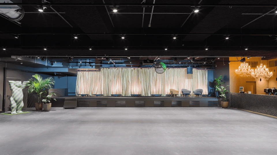 Moderne Veranstaltungshalle mit beleuchteter Bühne, großem Vorhang und Sitzreihen, umgeben von stilvoller Dekoration und Beleuchtung.