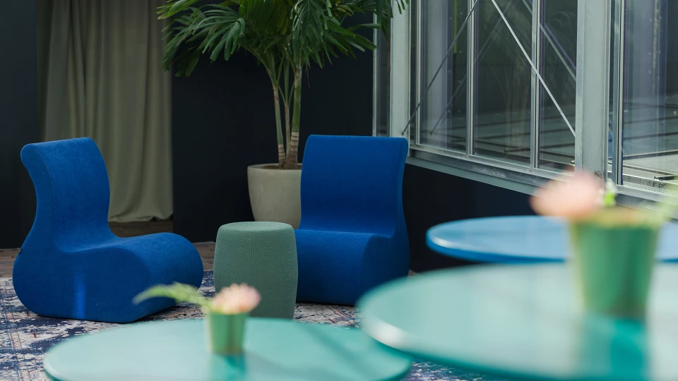 Ein modernes Wohnzimmer mit blauen und grünen Sesseln, einem großen Fenster und einer Zimmerpflanze