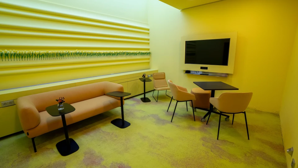 Design meeting room with a yellow lounge area, a large wall mural of artificial tulips, multiple seating options and a wall-mounted TV, ideal for creative workshops at Smartvillage Bogenhausen