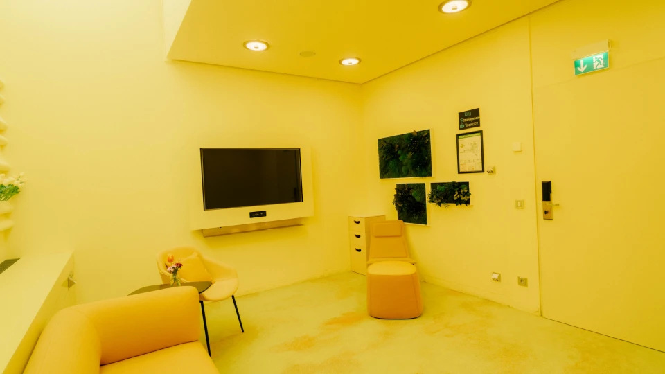Minimalist meeting room featuring a modern seating arrangement with a yellow designer armchair, a matching footstool, and a wall adorned with vibrant plant pictures – part of the Smartvillage concept
