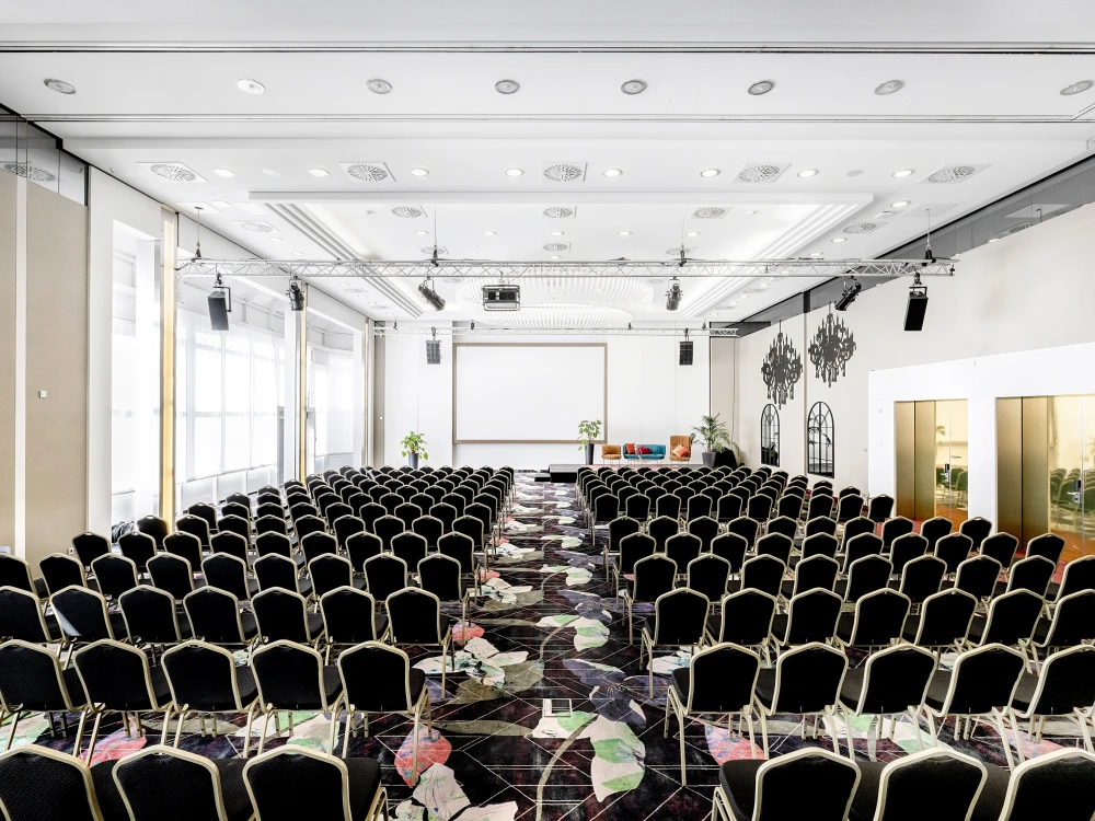Heller und stilvoller Konferenzsaal mit moderner Bestuhlung, großem Projektionsbildschirm und eleganter Beleuchtung. Perfekt für Tagungen, Präsentationen und Business-Events