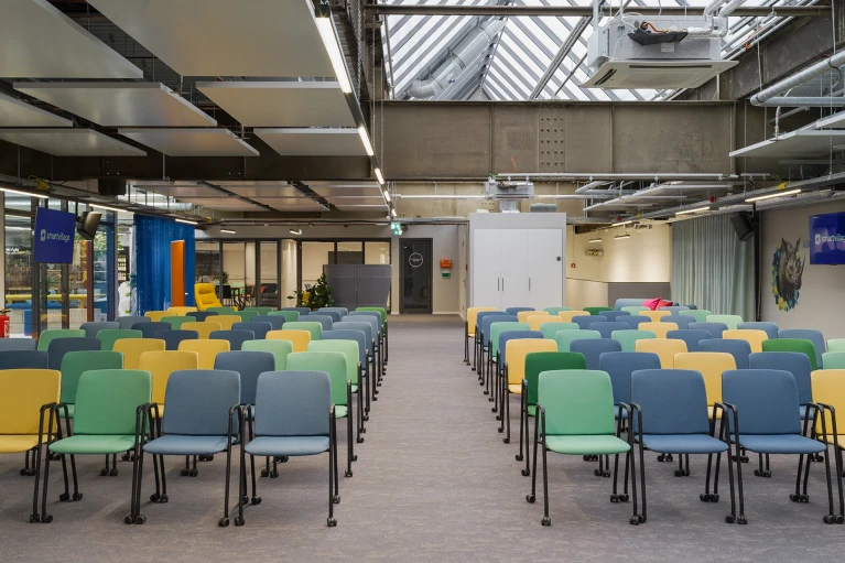Event space with a glass roof and colorful chairs at Smartvillage Cologne Mülheim