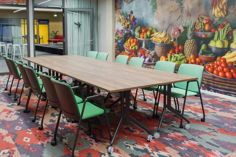 Colombia Bogota conference room featuring a large wooden table, green chairs, and a mural of a fruit and vegetable market, with a view towards the Uruguay area in Smartvillage
