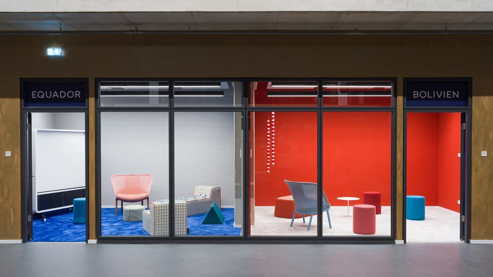 Sitzgruppe im Raum Bolivien mit blauem Loungesessel, bunten Hockern und Ausblick in die offene Coworking-Area des Smartvillage Köln