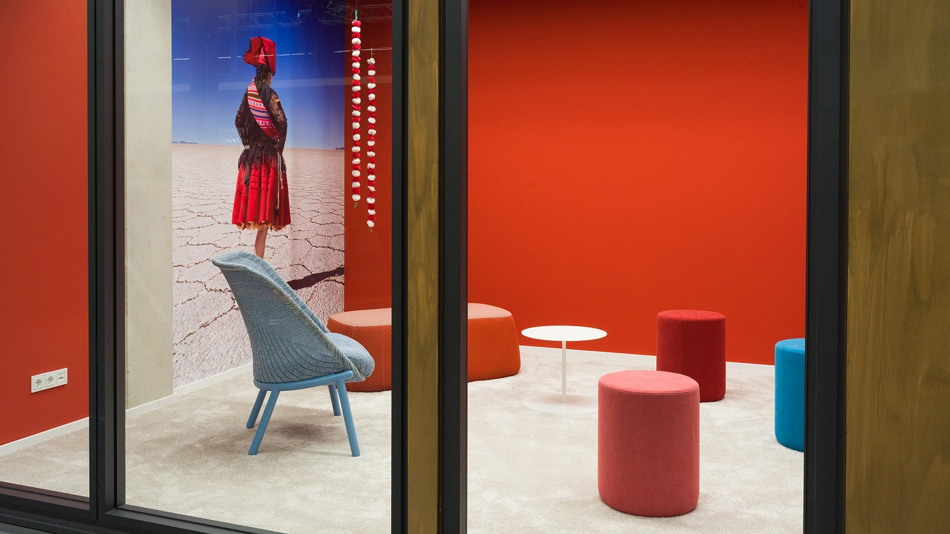 The 'Bolivia' room in Smartvillage Cologne featuring colorful lounge furniture, a glass door, and a cozy carpeted area