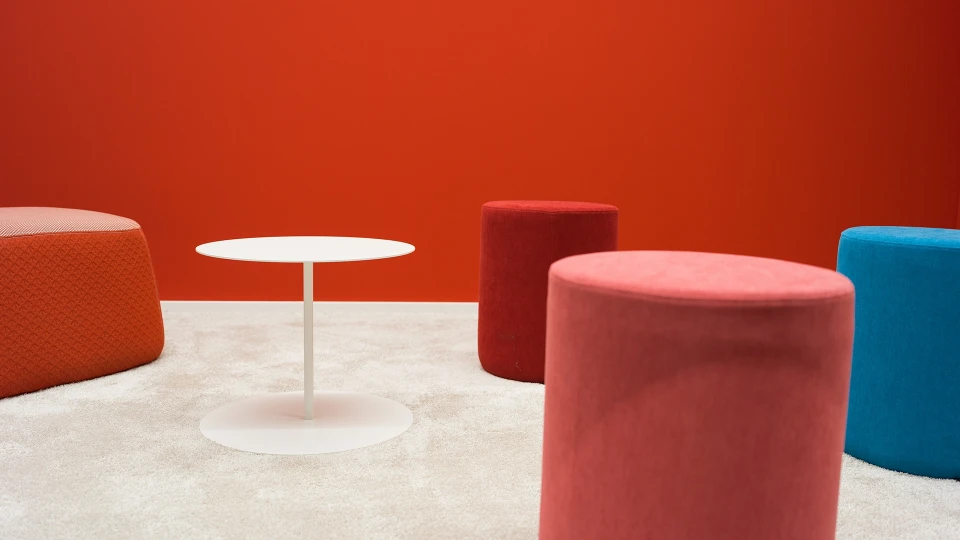 Sitzbereich im Raum Bolivien mit roten und blauen Hockern, hellen Teppichboden und roter Akzentwand im Smartvillage Köln