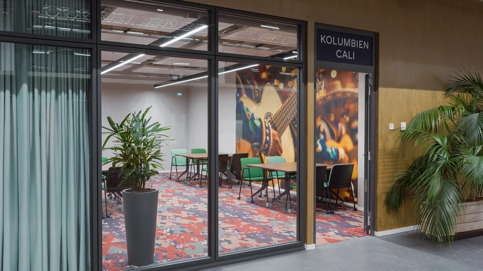 Besprechungsraum Kolumbien Cali mit grünem Mobiliar, farbenfrohem Teppich und Gitarren-Wandbild im Hintergrund
