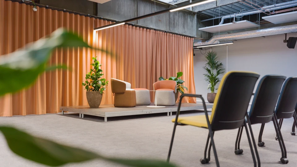 Nahaufnahme der Bühne mit zwei modernen Sesseln vor orangenen Vorhängen und umgeben von Pflanzen.