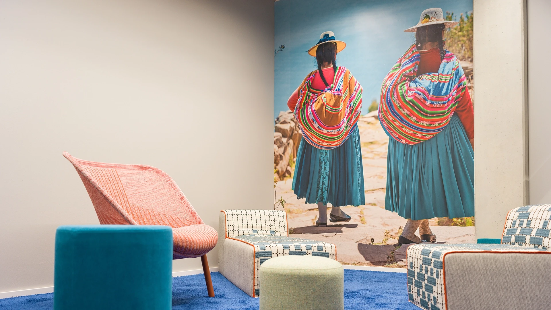 Gemütlicher Meetingraum mit buntem Teppich, kreativen Sitzmöbeln und Wandbild traditionell gekleideter Frauen vor See.
