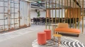 Modernes Büro mit einer Kombination aus rustikalen Containerwänden und stilvollen Möbeln, darunter ein orangefarbenes Sofa, runde rosa Hocker und ein schwarz-weißer Teppich.
