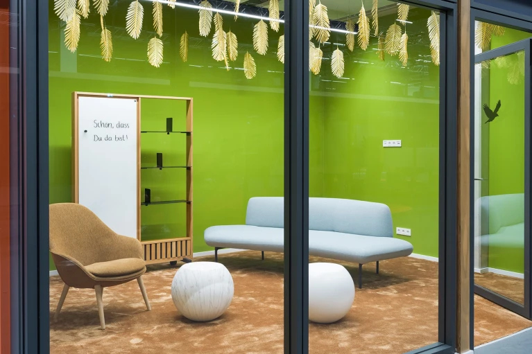 Interior view of the 'Guyana' meeting room featuring a green-painted wall, light blue couch, brown armchair, and white spherical stools.