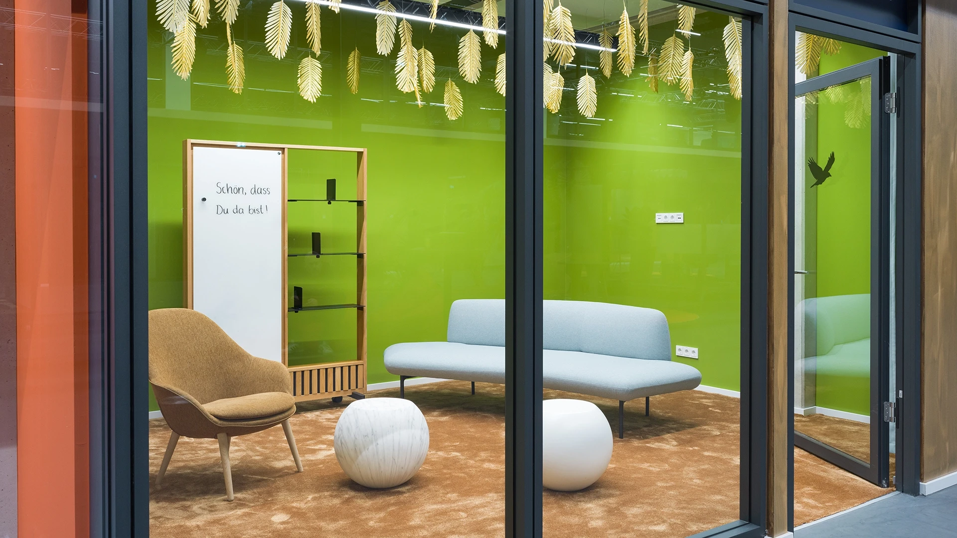 Innenansicht des Besprechungsraums "Guyana" mit grün gestrichener Wand, hellblauer Couch, braunem Sessel und weißen Kugelhockern.