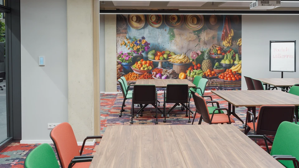 Totale des kombinierten Seminarraums „Kolumbien Bogotá & Cali“ mit mittigem Pfeiler, Teppich im Ethno-Stil und Sicht auf beide Wandbilder.