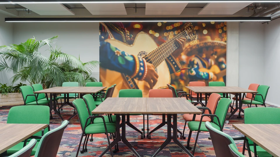 Perspektive auf den Cali-Teil des Raums mit großflächiger Gitarrenfotografie, umrahmt von grünen Pflanzen und farbigen Stühlen.