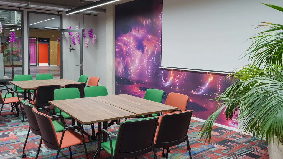 Modernes Besprechungszimmer mit einem großen Tisch und grünen Stühlen, umgeben von einer lebhaften Galaxie-Themenwand und einer Pflanze