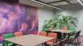 Besprechungsraum mit mehreren Tischen und Stühlen in Grün und Orange. Eine Wand ist mit einem großen Wandbild eines dramatischen lila Himmels mit Blitzen verziert.