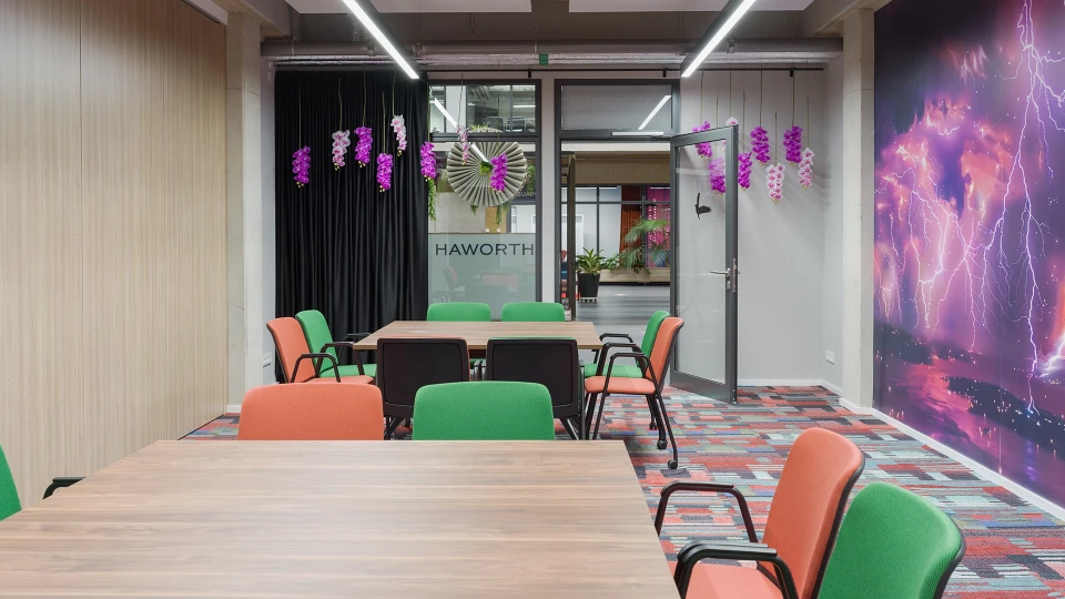 Modernes Büro mit bunten Stühlen um Holztische, dekoriert mit hängenden Pflanzen und einer Galaxie-Tapete an der Wand