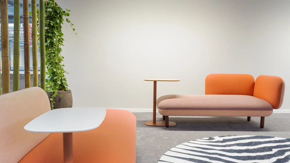 Zwei gepolsterte Loungesofas in Orange und Rosé mit kleinen Beistelltischen, Bambusdeko und hängender Pflanze im Hintergrund.