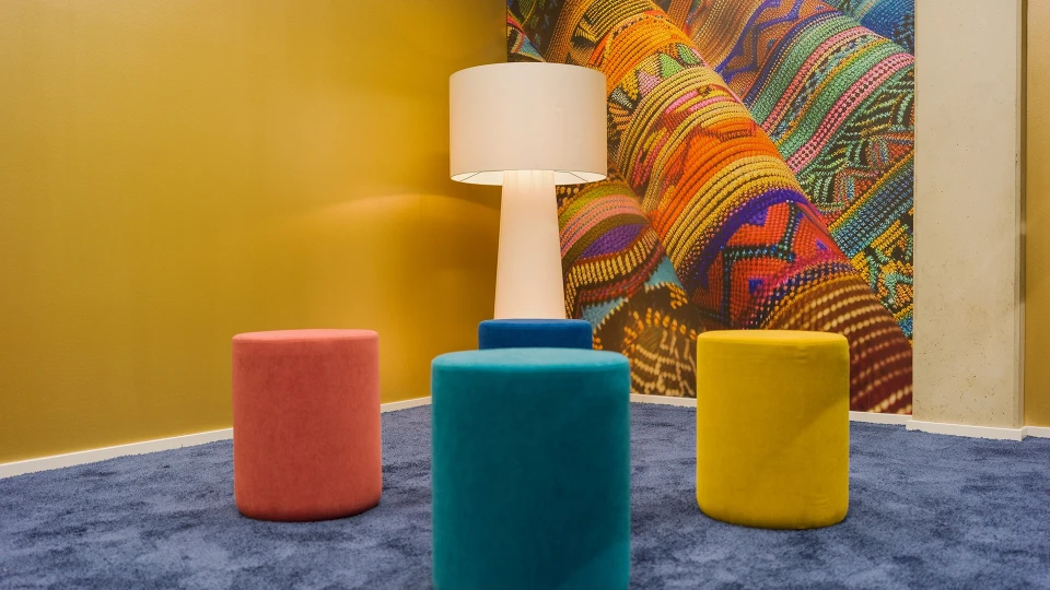 Exterior view of the 'Paraguay' meeting room featuring a large glass front, flipchart, and colorful decor with carpet and stools.