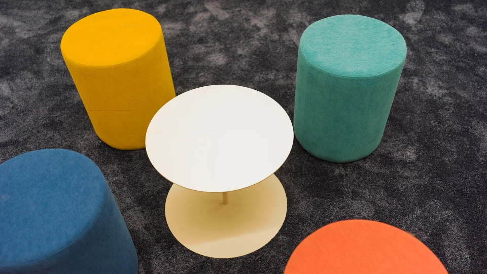 Colored stools and a white, round side table on a dark carpet viewed from above in the 'Paraguay' room.