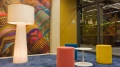 View through the window facade into the 'Paraguay' meeting room, featuring colorful wall design, blue carpet, and multicolored stools.