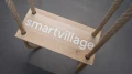 Close-up of a wooden swing with the inscription "smartvillage" on the seat.