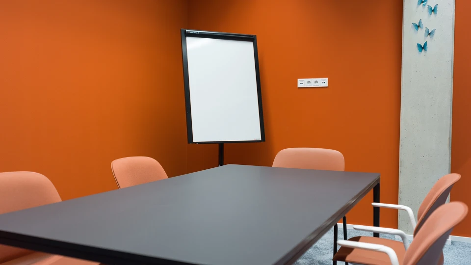 Interior view of the 'Suriname' meeting room featuring orange chairs, a table, and a flipchart.