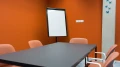 Interior view of the 'Suriname' meeting room featuring orange chairs, a table, and a flipchart.