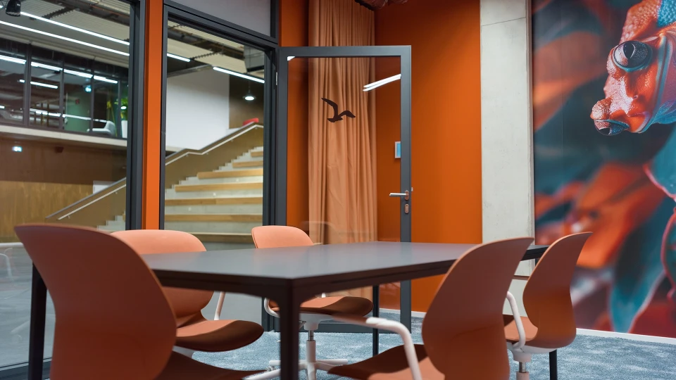 View of the door and table in the 'Suriname' meeting room, with a view into the atrium and wall art.