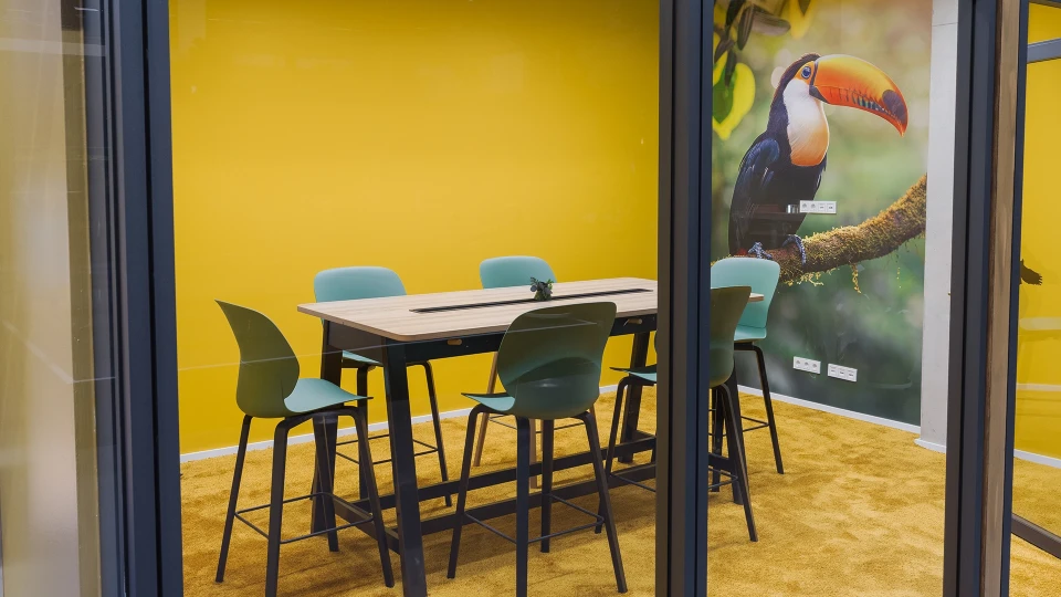 Meeting area with a yellow wall and a large toucan design in the Uruguay room at smartvillage Cologne-Muelheim.