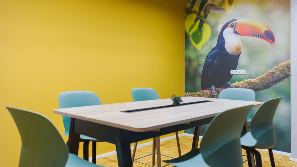 Bright meeting room with a yellow wall, light blue chairs, and a flipchart in smartvillage Cologne-Muelheim.