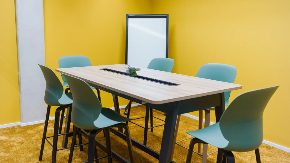 Close-up of a meeting table with a plant in the foreground, located in the 'Uruguay' room of smartvillage Cologne Mülheim.
