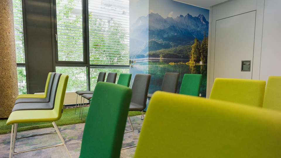 Modernes Wartezimmer mit grünen und grauen Stühlen, großes Bergpanorama-Fototapete an der Wand, Blick auf Fenster mit Jalousien