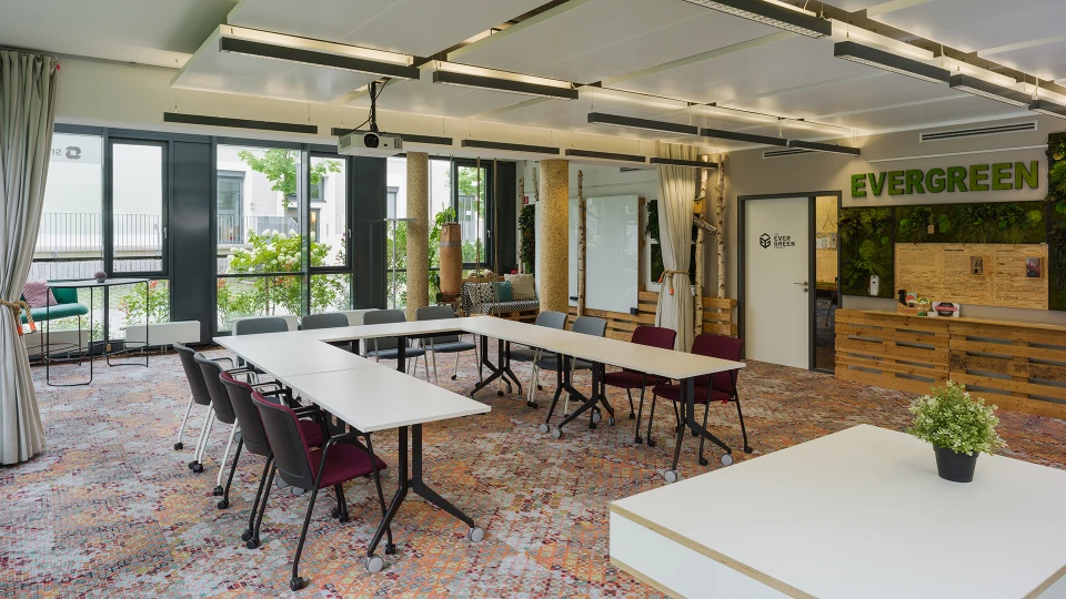 Modern office with multiple white tables and dark red chairs, a reception area labeled 'EVERGREEN', and green wall decor.