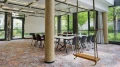Modern office with a long conference table surrounded by chairs, a swing, and large windows overlooking green trees.