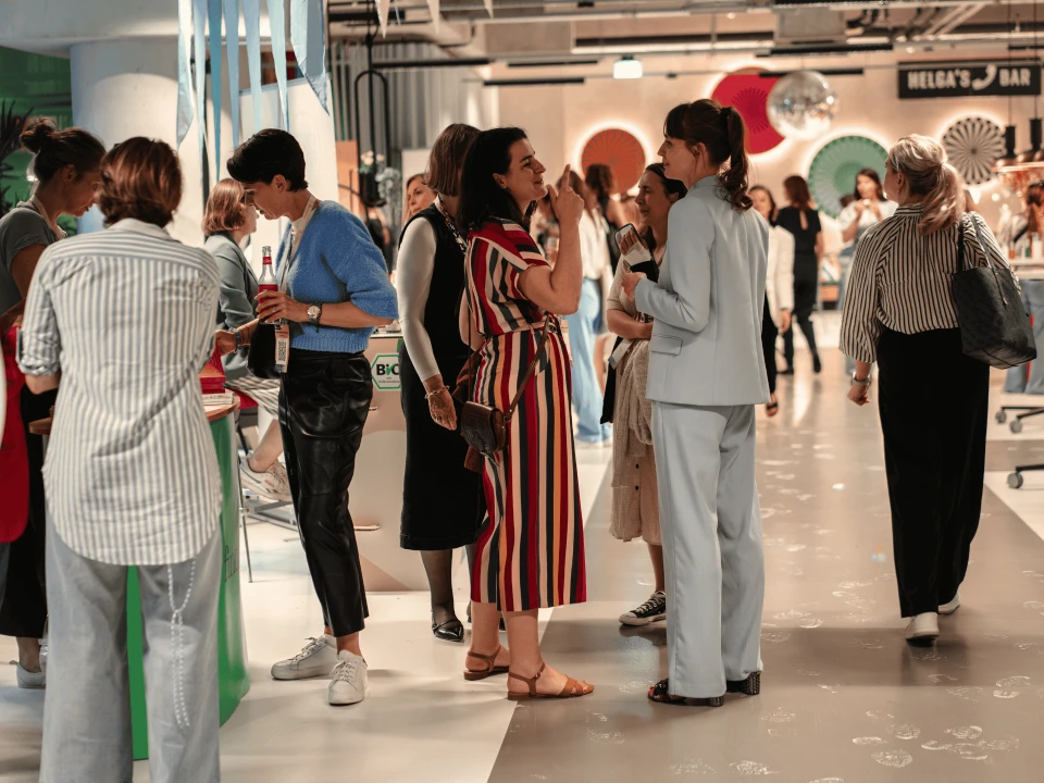 People interacting at a social event in a busy indoor setting with modern, colorful decor