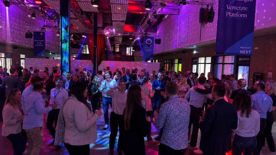Eine Gruppe von Menschen bei einer Netzwerkveranstaltung in einer beleuchteten Halle mit bunten Lichtern und Bannern.